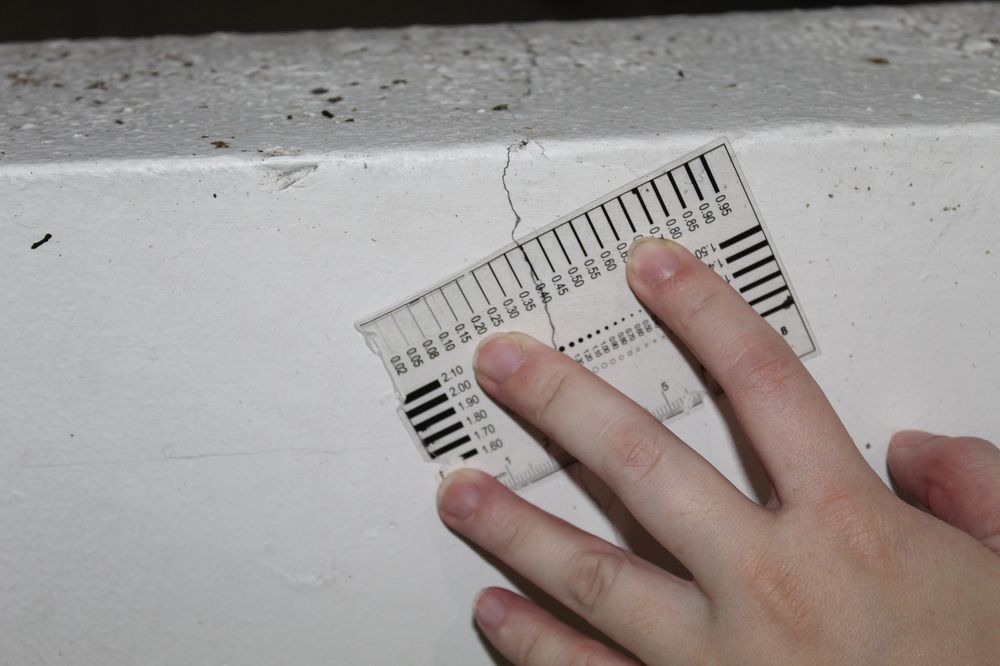 Crack width comparator card held against a concrete wall